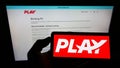 Person holding mobile phone with logo of Icelandic low-cost airline company Fly Play hf. on screen in front of web page.