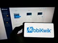 Person holding mobile phone with logo of Indian financial technology company MobiKwik on screen in front of business webpage.