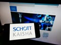 Person holding mobile phone with logo of Indian packaging company Schott Kaisha Pvt. Ltd. on screen in front of web page. Royalty Free Stock Photo