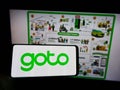 Person holding mobile phone with logo of Indonesian company GoTo Group on screen in front of business web page.