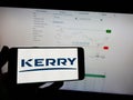 Person holding mobile phone with logo of Irish food company Kerry Group plc on screen in front of business web page.
