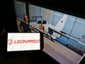 Person holding mobile phone with logo of Italian defense company Leonardo S.p.A. on screen in front of business webpage.