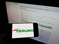 Person holding mobile phone with logo of Japanese medical equipment company Terumo Corp. on screen in front of web page.