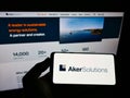 Person holding mobile phone with logo of Norwegian engineering company Aker Solutions ASA on screen in front of web page.