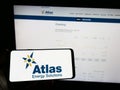 Person holding mobile phone with logo of oil and gas company Atlas Energy Solutions Inc. on screen in front of web page.