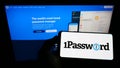 Person holding mobile phone with logo of password manager company AgileBits Inc. (1Password) on screen with web page.