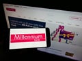 Person holding mobile phone with logo of Polish financial company Bank Millennium SA on screen in front of business webpage.