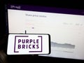 Person holding mobile phone with logo of real estate company Purplebricks Group plc on screen in front of web page. Royalty Free Stock Photo