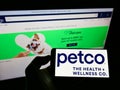 Person holding mobile phone with logo of retailer Petco Health and Wellness Company Inc. on screen in front of web page.