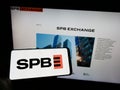 Person holding mobile phone with logo of Russian financial marketplace SPB Exchange on screen in front of web page.