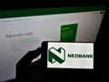 Person holding mobile phone with logo of South African bank Nedbank Group Limited on screen in front of business web page.