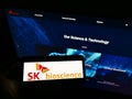 Person holding mobile phone with logo of South Korean biological company SK Bioscience Co Ltd on screen in front of webpage.