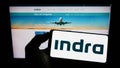 Person holding mobile phone with logo of Spanish company Indra Sistemas S.A. on screen in front of business web page.