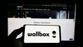 Person holding mobile phone with logo of Spanish energy company Wallbox Charger S.L. on screen in front of web page.