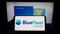 Person holding mobile phone with logo of Spanish renewables company BlueFloat Energy LLC on screen in front of web page.