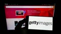 Person holding mobile phone with logo of stock photo provider Getty Images Inc. on screen in front of business web page.