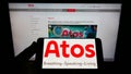 Person holding mobile phone with logo of Swedish medical technology company Atos Medical AB on screen in front of web page.