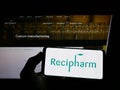 Person holding mobile phone with logo of Swedish pharmaceutical Recipharm AB on screen in front of business web page.