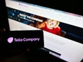 Person holding mobile phone with logo of Swedish telecommuncations provider Telia Company AB on screen in front of web page.