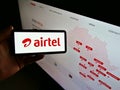 Person holding mobile phone with logo of telecommunications provider Airtel Africa plc on display in front of company website.