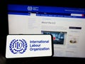 Person holding mobile phone with logo of UN agency International Labour Organization (ILO) on screen with web page.