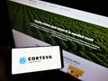 Person holding mobile phone with logo of US agricultural chemical company Corteva Agriscience on screen in front of web page.