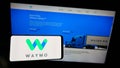 Person holding mobile phone with logo of US autonomous driving company Waymo LLC on screen in front of business web page.