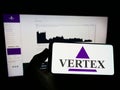 Person holding mobile phone with logo of US company Vertex Pharmaceuticals Inc. on screen in front of business web page. Royalty Free Stock Photo