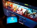 Person holding mobile phone with logo of US distribution platform Steam operated by Valve on screen in front of web page.