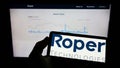 Person holding mobile phone with logo of US engineering company Roper Technologies Inc. on screen in front of web page. Royalty Free Stock Photo