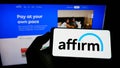 Person holding mobile phone with logo of US financial technology company Affirm Holdings Inc. on screen in front of webpage.