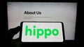 Person holding mobile phone with logo of US insurance company Hippo Holdings Inc. on screen in front of business web page.