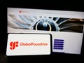 Person holding mobile phone with logo of US semiconductor company GlobalFoundries Inc. (GF) on screen with web page.