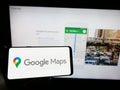 Person holding mobile phone with logo of web mapping platform Google Maps on screen in front of web page.