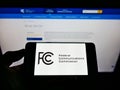 Person holding mobile phone with seal of US agency Federal Communications Commission (FCC) on screen with web page.