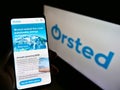Person holding mobile phone with webpage of Danish power company ÃËrsted AS on screen in front of logo.