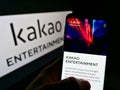 Person holding mobile phone with webpage of South Korean company Kakao Entertainment Corp. on screen with logo.