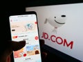 Person holding mobile phone with website of Chinese e-commerce company JD.com Inc. on screen in front of logo.