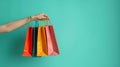 Person holding multiple vibrant shopping bags against a bright teal backdrop with copy space Royalty Free Stock Photo