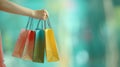 Person holding multiple vibrant shopping bags against a bright teal backdrop with copy space Royalty Free Stock Photo