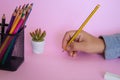 Person holding a pencil next to the colorful pencils in the metal mesh pencil cup holder Royalty Free Stock Photo