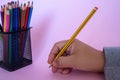 Person holding a pencil next to the colorful pencils in the metal mesh pencil cup holder Royalty Free Stock Photo