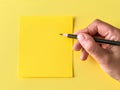 A person holding a pencil and writing on a yellow note Royalty Free Stock Photo