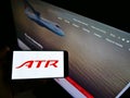 Person holding phone with logo of aircraft manufacturer Avions de Transport RÃÂ©gional (ATR) on screen with web page.