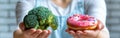 A person holding a pink doughnut in one hand and a piece of broccoli in the other hand Royalty Free Stock Photo