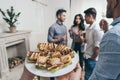 Person holding plate with tasty sandwiches while smiling young friends drinking champagne behind Royalty Free Stock Photo