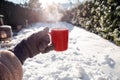 Person holding a red mug with hot coffee,tea or Chocolate milk with steaming smoke and gloves in the snow, Winter