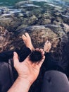 Person holding a sea urchin in their palm while their feet are submerged in a rocky water