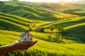 A person holding a small house in front of a green field Royalty Free Stock Photo