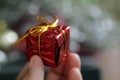 Person holding small red gift box in hand with ribbon on blur bokeh Christmas decoration Royalty Free Stock Photo